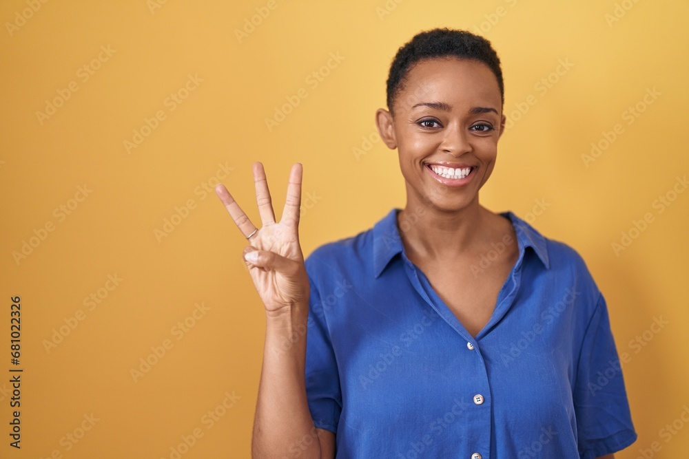 African american woman standing over yellow background showing and pointing up with fingers number three while smiling confident and happy. African american woman standing over yellow background showing and pointing up with fingers number three while smiling confident and happy.