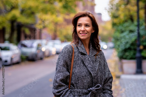Brunette haired woman wearing tweed coat and walking outdoors in the city street on autumn day