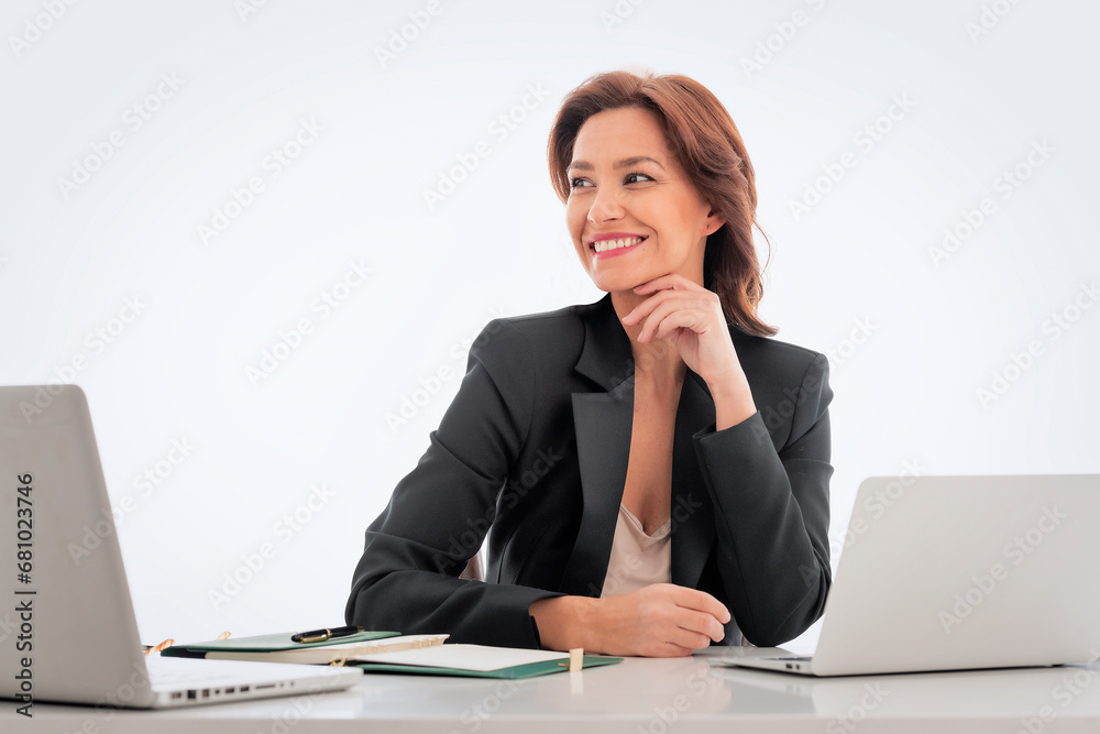 Mid age businesswoman sitting at desk against isolated background and using laptops Mid age businesswoman sitting at desk against isolated background and using laptops