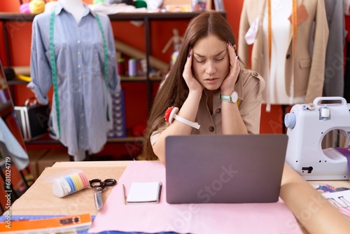 Young beautiful woman tailor stressed using laptop at atelier
