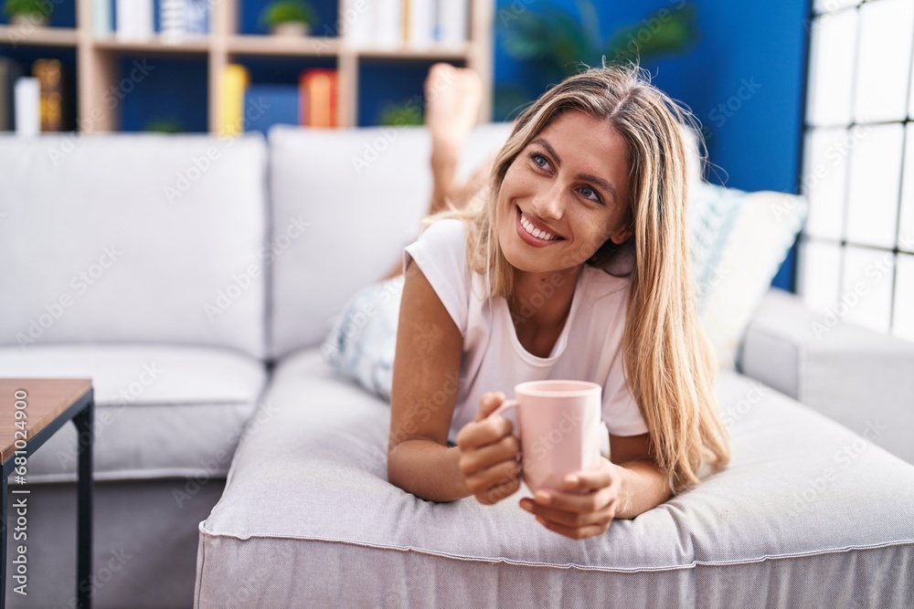 Young blonde woman drinking coffee lying on sofa at home Young blonde woman drinking coffee lying on sofa at home