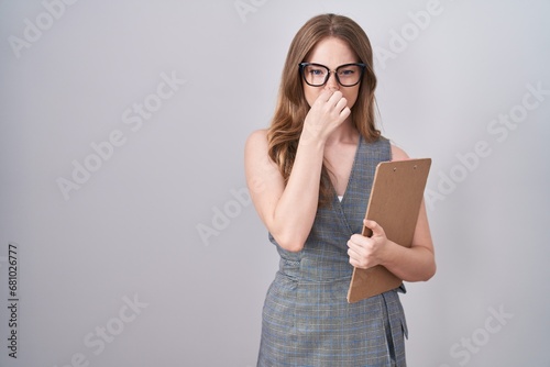Caucasian woman wearing glasses and business clothes smelling something stinky and disgusting, intolerable smell, holding breath with fingers on nose. bad smell