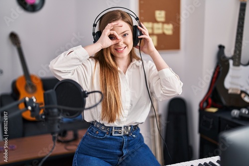 Young caucasian woman recording song at music studio smiling happy doing ok sign with hand on eye looking through fingers