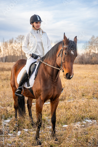 Beautiful blond professional female jockey riding a horse in field