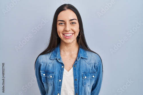 Hispanic woman standing over blue background with a happy and cool smile on face. lucky person.
