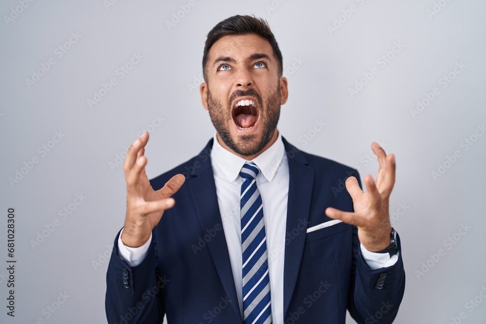 Handsome hispanic man wearing suit and tie crazy and mad shouting and yelling with aggressive expression and arms raised. frustration concept. Handsome hispanic man wearing suit and tie crazy and mad shouting and yelling with aggressive expression and arms raised. frustration concept.