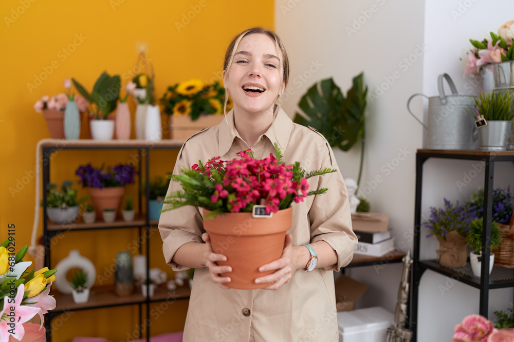 Young caucasian woman working at florist shop holding plant pot smiling and laughing hard out loud because funny crazy joke.