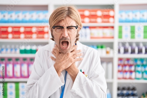 Caucasian man with mustache working at pharmacy drugstore shouting and suffocate because painful strangle. health problem. asphyxiate and suicide concept.