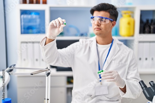 Young hispanic man scientist holding pill with hand at street