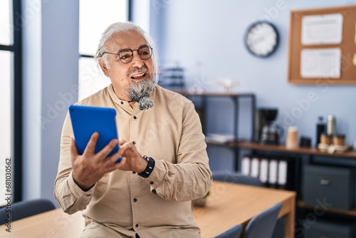 Middle age grey-haired man business worker smiling confident using touchpad at office