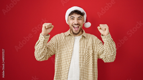 Young arab man wearing christmas hat with cheerful expression over isolated red background