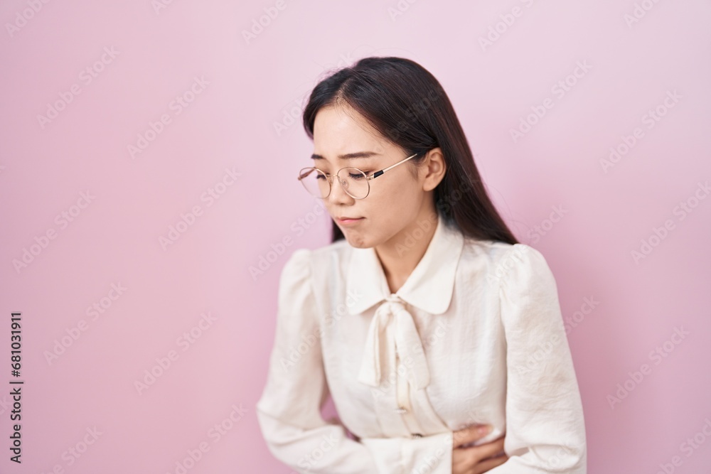 Young chinese woman standing over pink background with hand on stomach because nausea, painful disease feeling unwell. ache concept. Young chinese woman standing over pink background with hand on stomach because nausea, painful disease feeling unwell. ache concept.