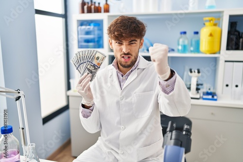 Arab man with beard working at scientist laboratory holding money annoyed and frustrated shouting with anger  yelling crazy with anger and hand raised