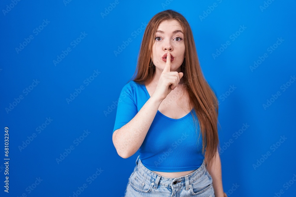 Redhead woman standing over blue background asking to be quiet with finger on lips. silence and secret concept. Redhead woman standing over blue background asking to be quiet with finger on lips. silence and secret concept.
