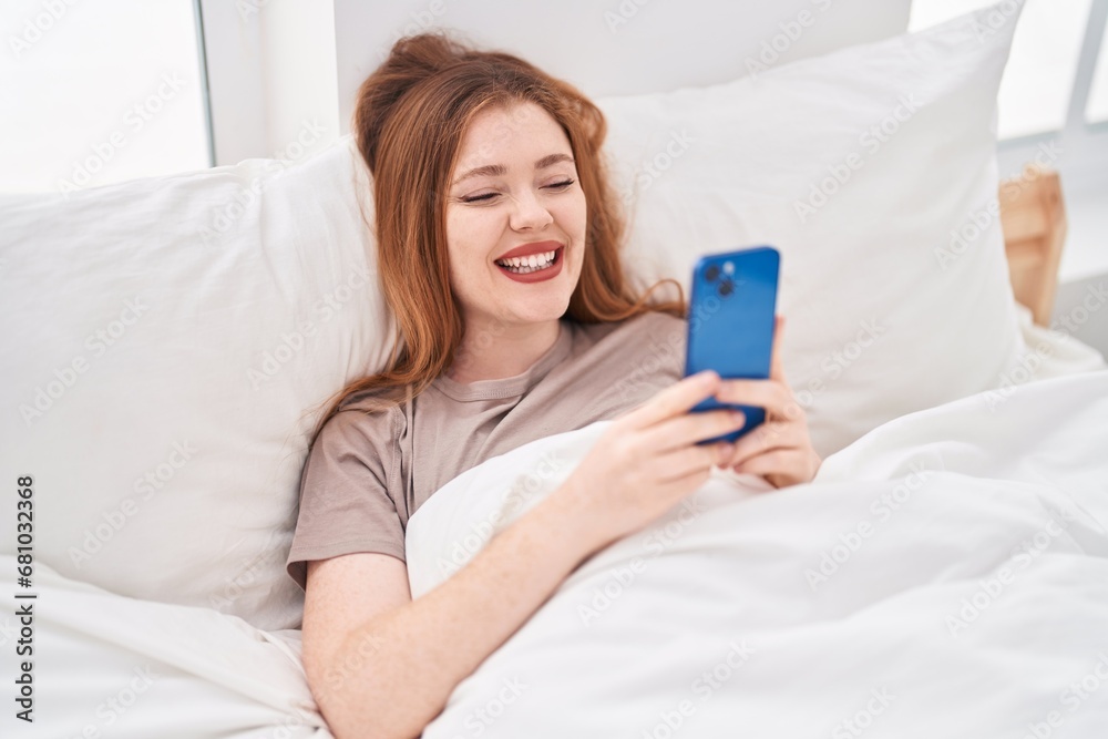 Young redhead woman using smartphone lying on bed at bedroom Young redhead woman using smartphone lying on bed at bedroom