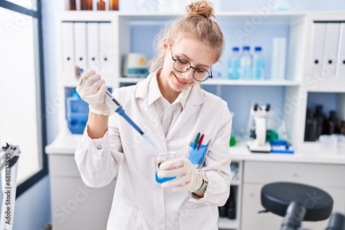 Young blonde woman scientist smiling confident pouring liquid on test tube at laboratory