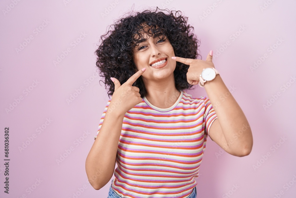 Young middle east woman standing over pink background smiling cheerful showing and pointing with fingers teeth and mouth. dental health concept. Young middle east woman standing over pink background smiling cheerful showing and pointing with fingers teeth and mouth. dental health concept.