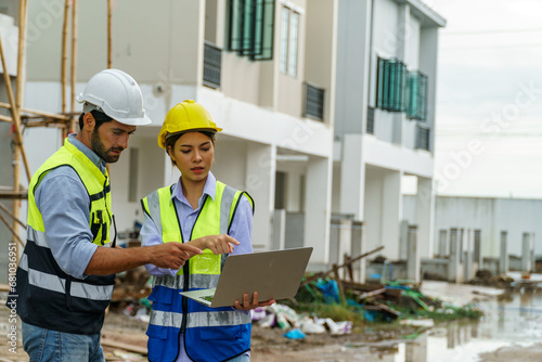 Foreman man and woman with Yellow helmet holding laptop in constuction site photo