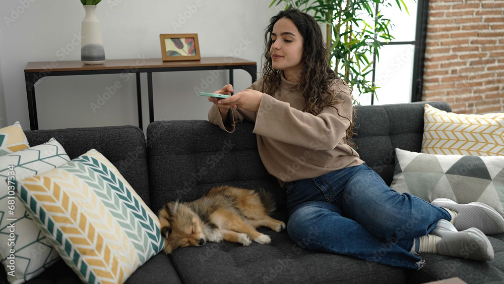 Young hispanic woman with dog make photo by smartphone to asleep dog at home