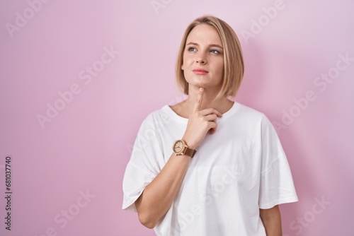 Young caucasian woman standing over pink background thinking concentrated about doubt with finger on chin and looking up wondering