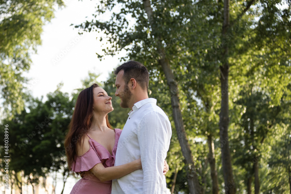 Lovely couple hugging in park. Portrait of attractive young cheerful pair lovers relaxing on summer forest background. Sweet family embracing outdoors. Charming spouses anniversary at picnic Lovely couple hugging in park. Portrait of attractive young cheerful pair lovers relaxing on summer forest background. Sweet family embracing outdoors. Charming spouses anniversary at picnic