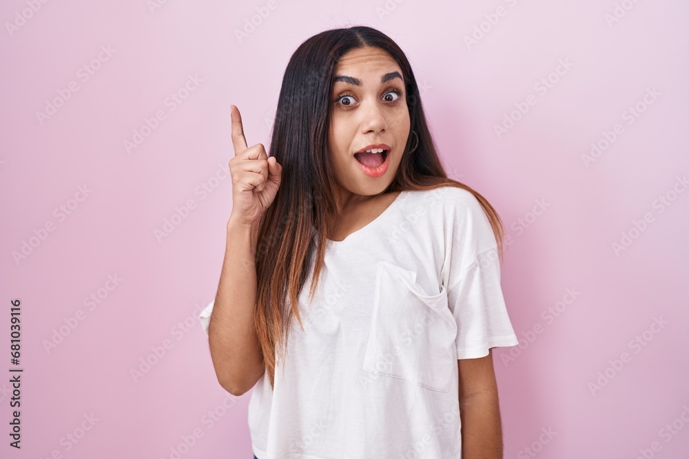 Young arab woman standing over pink background pointing finger up with successful idea. exited and happy. number one. Young arab woman standing over pink background pointing finger up with successful idea. exited and happy. number one.