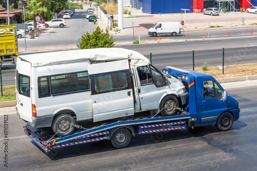 Dented twisted metal after an accident broken minibus on a tow truck on city street.