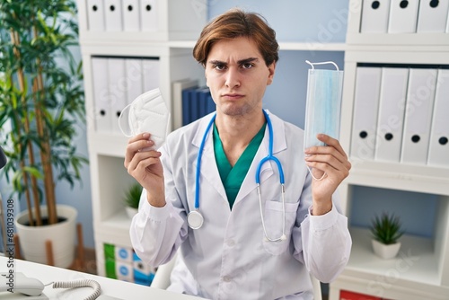 Young doctor man holding two safety mask skeptic and nervous, frowning upset because of problem. negative person. photo