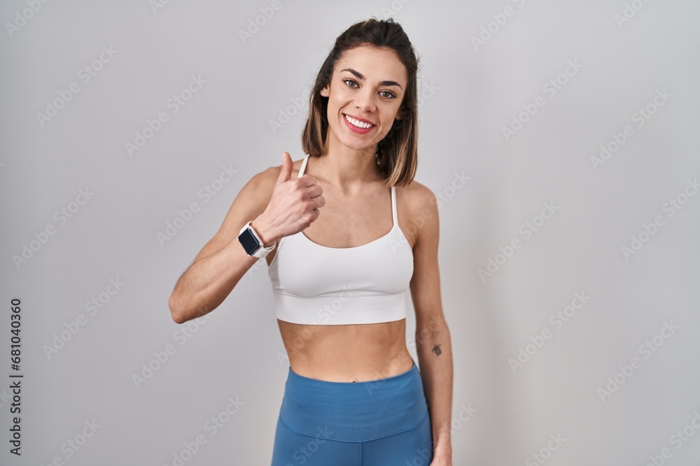 Hispanic woman wearing sportswear over isolated background doing happy thumbs up gesture with hand. approving expression looking at the camera showing success. Hispanic woman wearing sportswear over isolated background doing happy thumbs up gesture with hand. approving expression looking at the camera showing success.