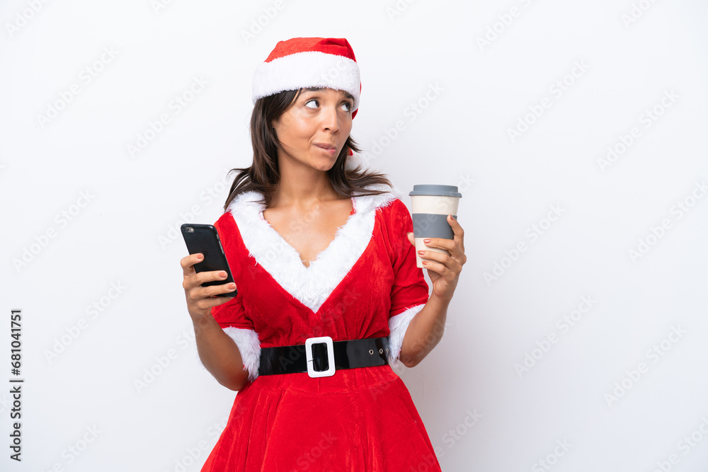 Young hispanic woman dressed as mama noel isolated on white background holding coffee to take away and a mobile while thinking something Young hispanic woman dressed as mama noel isolated on white background holding coffee to take away and a mobile while thinking something
