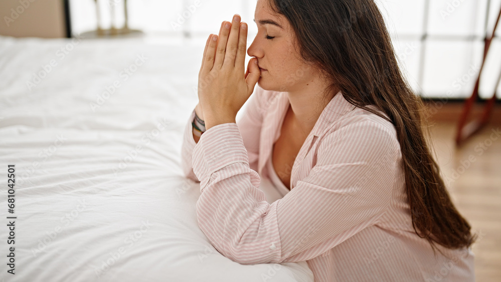 Young beautiful hispanic woman leaning on bed praying at bedroom Young beautiful hispanic woman leaning on bed praying at bedroom