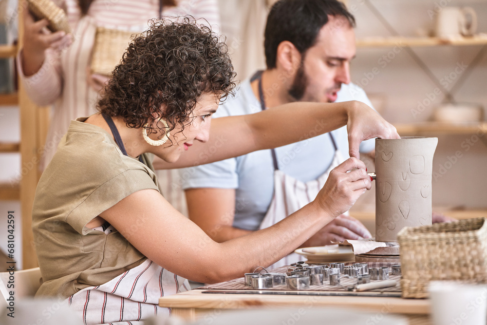 Woman decorating a ceramic vase while having a pottery class. Hobby and craft concept. - obrazy, fototapety, plakaty 