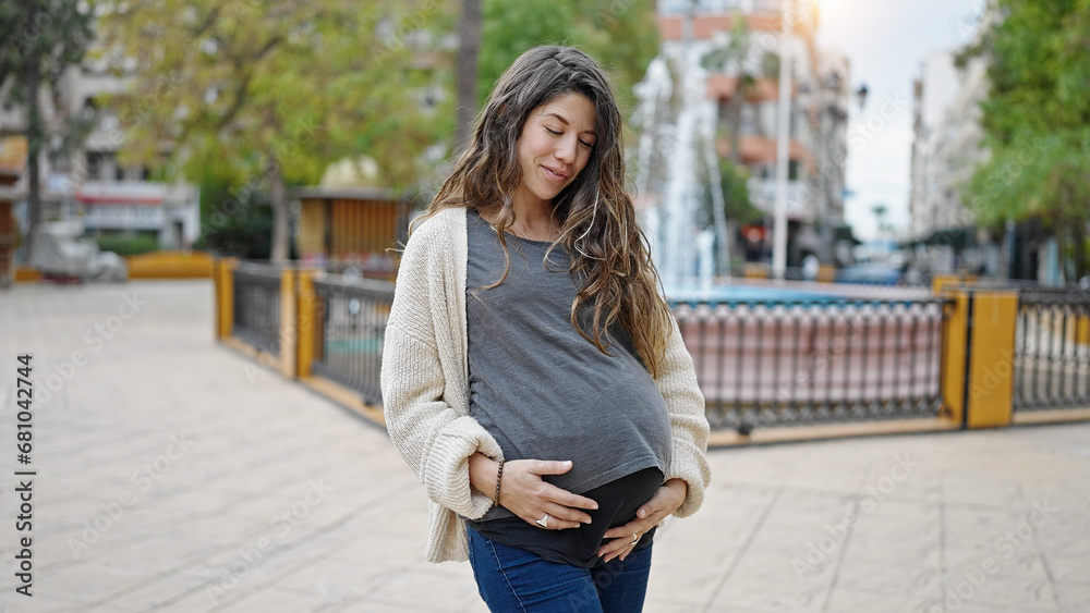 Young pregnant woman smiling confident touching belly at park