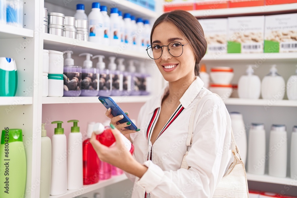 Young beautiful hispanic woman customer using smartphone holding medicine bottle at pharmacy Young beautiful hispanic woman customer using smartphone holding medicine bottle at pharmacy