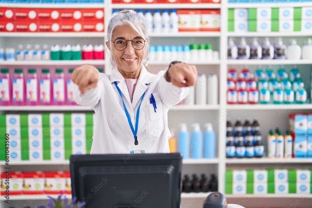 Middle age woman with tattoos working at pharmacy drugstore pointing to you and the camera with fingers, smiling positive and cheerful Middle age woman with tattoos working at pharmacy drugstore pointing to you and the camera with fingers, smiling positive and cheerful