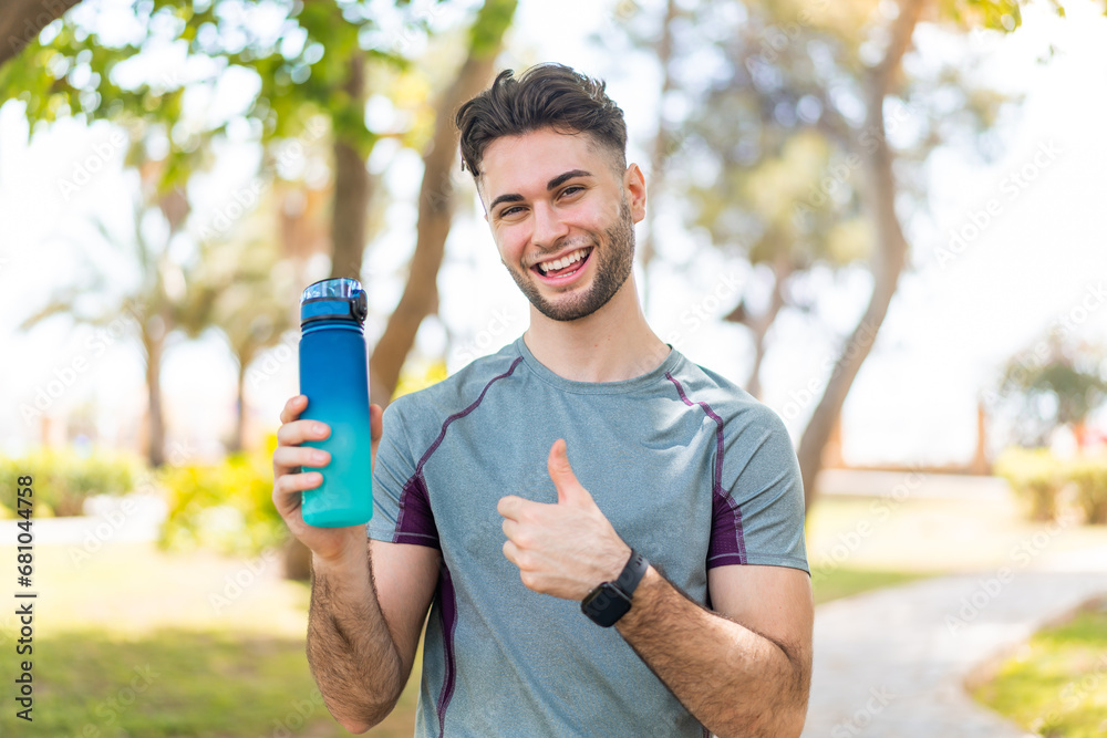 Young handsome sport man with a bottle of water at outdoors with thumbs up because something good has happened Young handsome sport man with a bottle of water at outdoors with thumbs up because something good has happened