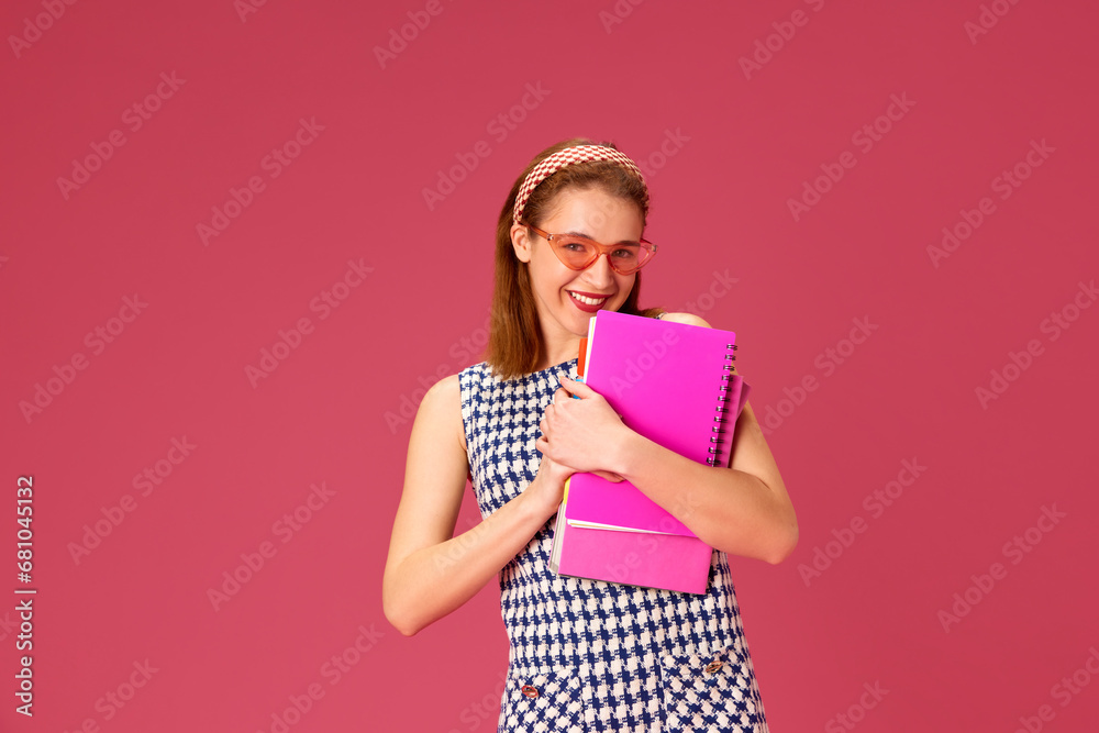 Beautiful, smiling young woman in pink sunglasses standing with notebooks against pink studio background. Freelancer. Concept of youth, human emotions, education, lifestyle, fashion Beautiful, smiling young woman in pink sunglasses standing with notebooks against pink studio background. Freelancer. Concept of youth, human emotions, education, lifestyle, fashion