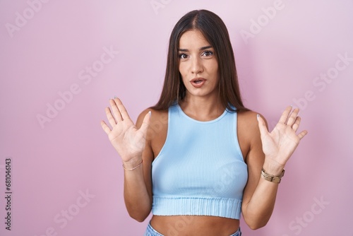 Young brunette woman standing over pink background moving away hands palms showing refusal and denial with afraid and disgusting expression. stop and forbidden. © Krakenimages.com