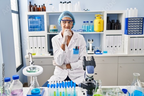 Brunette woman working at scientist laboratory thinking worried about a question, concerned and nervous with hand on chin