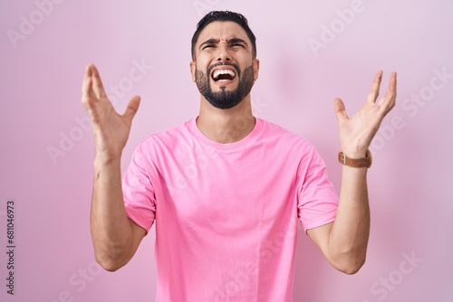 Hispanic young man standing over pink background crazy and mad shouting and yelling with aggressive expression and arms raised. frustration concept. photo
