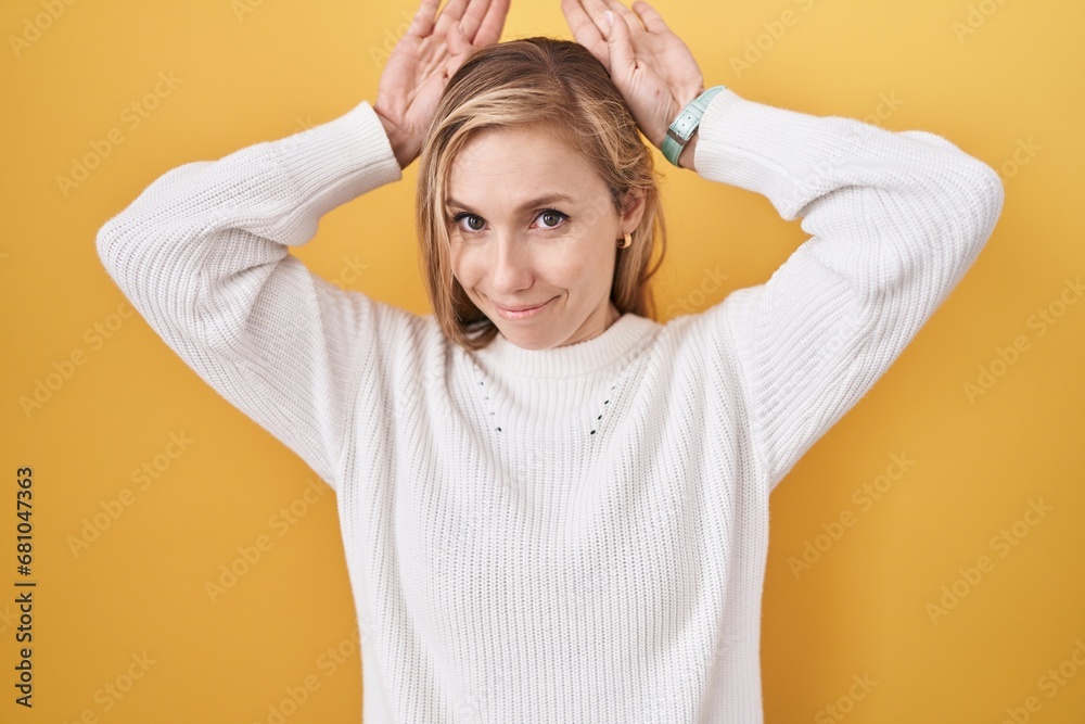 Young caucasian woman wearing white sweater over yellow background doing bunny ears gesture with hands palms looking cynical and skeptical. easter rabbit concept. Young caucasian woman wearing white sweater over yellow background doing bunny ears gesture with hands palms looking cynical and skeptical. easter rabbit concept.
