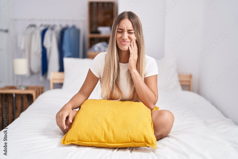 Φωτογραφία Young blonde woman sitting on the bed with pillow at home touching mouth with hand with painful expression because of toothache or dental illness on teeth