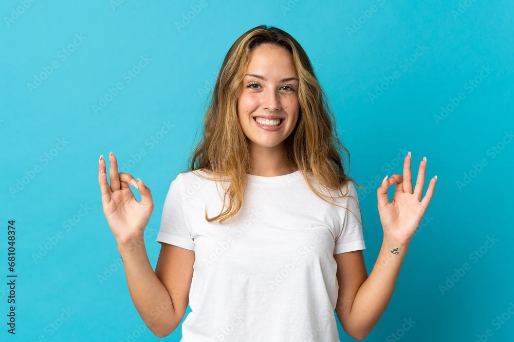 Young blonde woman isolated on blue background showing an ok sign with fingers Young blonde woman isolated on blue background showing an ok sign with fingers