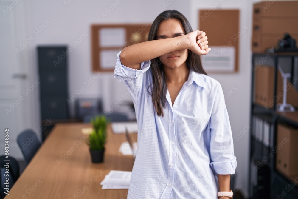 Young hispanic woman at the office covering eyes with arm, looking serious and sad. sightless, hiding and rejection concept Young hispanic woman at the office covering eyes with arm, looking serious and sad. sightless, hiding and rejection concept