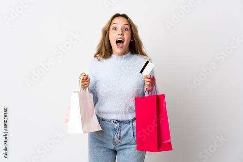 Young blonde woman isolated on white background holding shopping bags and surprised