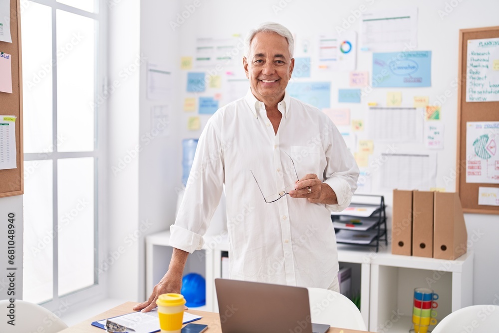 Middle age grey-haired man business worker smiling confident standing by desk at office