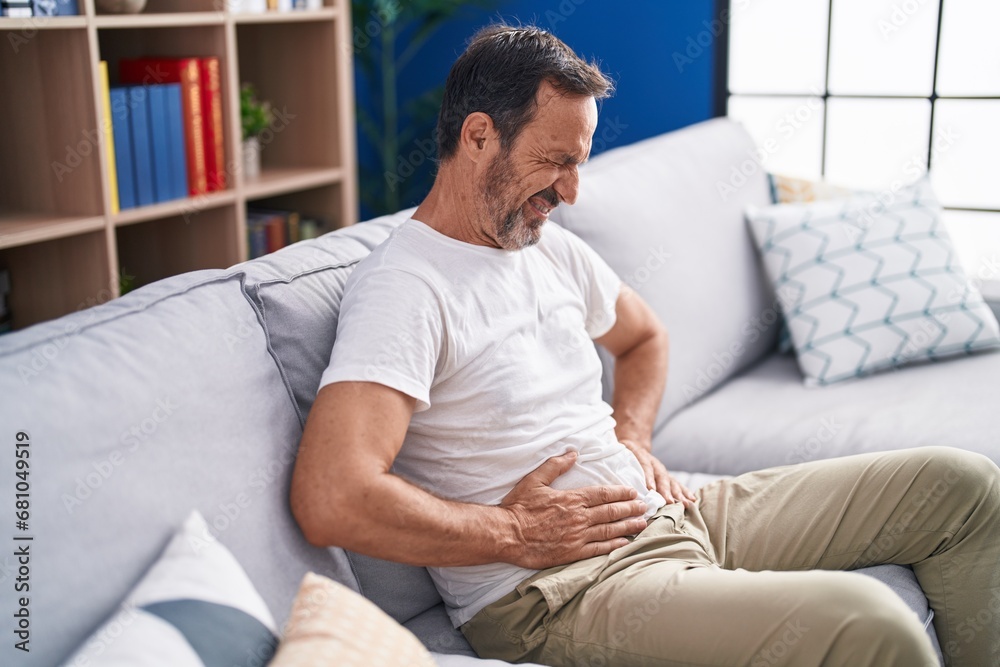 Middle age man suffering for stomach ache sitting on sofa at home