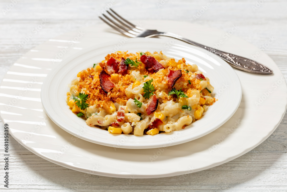 portion of mac and cheese with corn, bacon topped with panko breadcrumbs on white plate on white wooden table, horizontal view from above, close-u portion of mac and cheese with corn, bacon topped with panko breadcrumbs on white plate on white wooden table, horizontal view from above, close-u