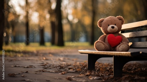 A forgotten toy bear with red heart lies on bench in an empty autumn park. Concept of Loneliness, solitude, autumn nostalgia.