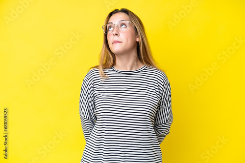 Young caucasian woman isolated on yellow background and looking up